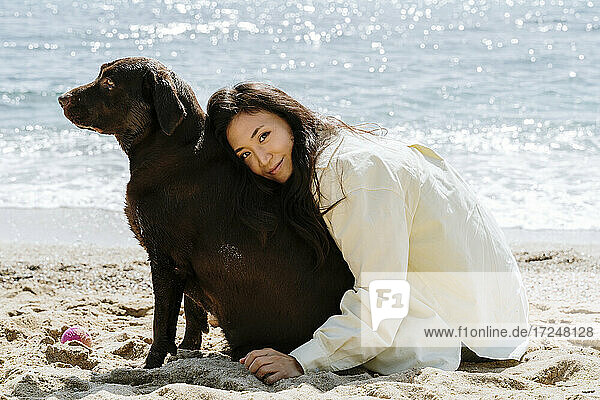 Schöne Frau umarmt Hund auf Sand während sonnigen Tag