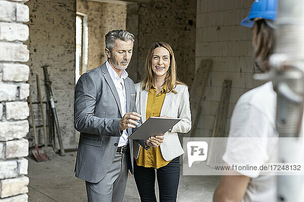 Male architect with digital tablet standing by smiling female colleague at site