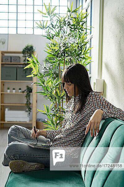 Weibliche Grafikdesignerin benutzt ein Tablet  während sie auf dem Sofa im Büro sitzt