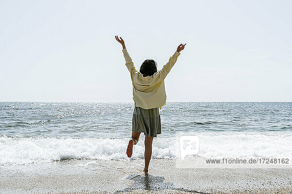 Frau mit erhobenen Armen am Strand stehend an einem sonnigen Tag