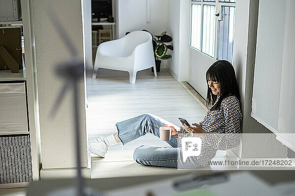 Berufstätige Frau benutzt ihr Smartphone  während sie sich im Büro an eine Säule lehnt