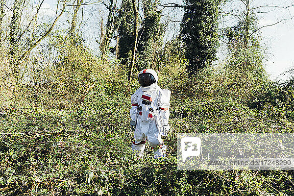 Junger Astronaut mit Raumanzug und Helm steht im Busch im Wald
