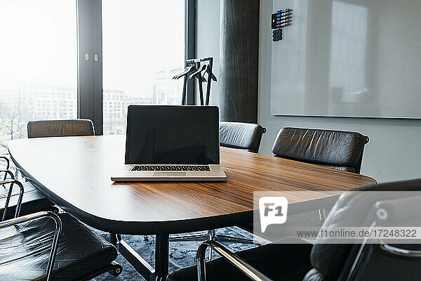 Leerer Laptop auf Konferenztisch inmitten von Stühlen im Büro