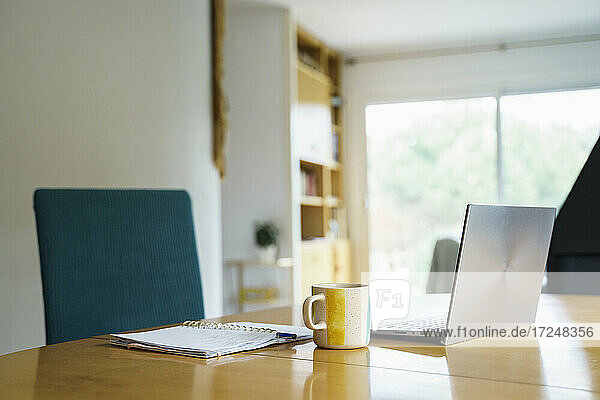 Laptop mit Kaffeetasse und Buch auf dem Tisch zu Hause