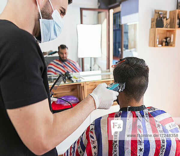 Male hairstylist cutting hair of customer with machine at barber shop