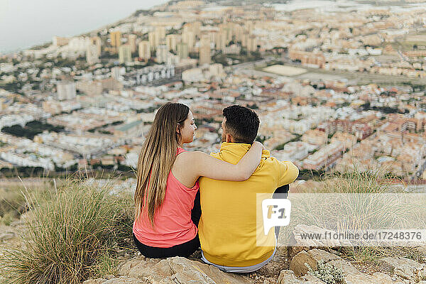 Junge Freundin sitzt mit dem Arm um ihren Freund auf einem Hügel