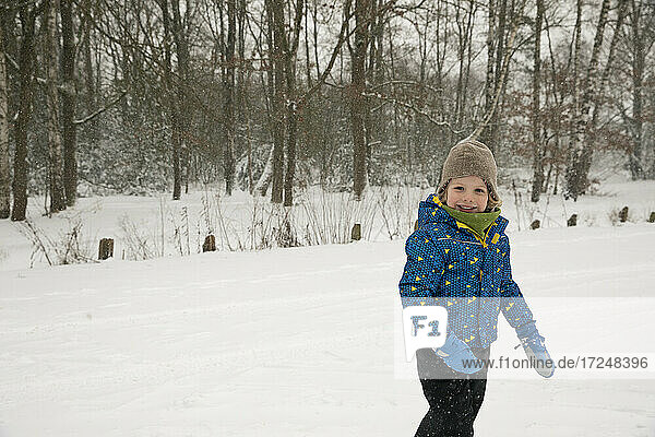 Lächelnder Junge in warmer Kleidung  der im Winter im Schnee steht