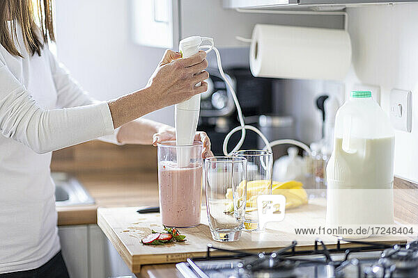 Frau bereitet Erdbeermilchshake mit Gläsern in der Küche zu