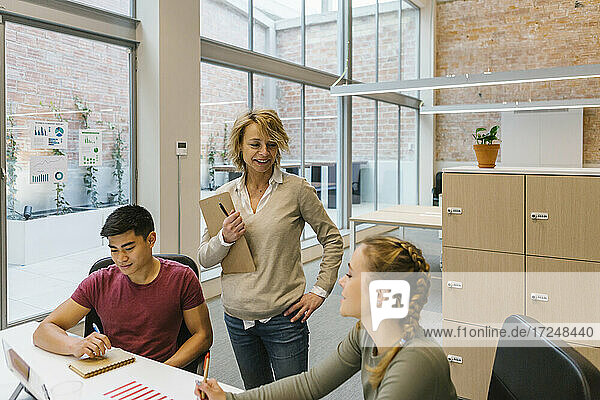 Lächelnde weibliche Fachkräfte  die mit einem männlichen Kollegen in einem Coworking-Büro diskutieren