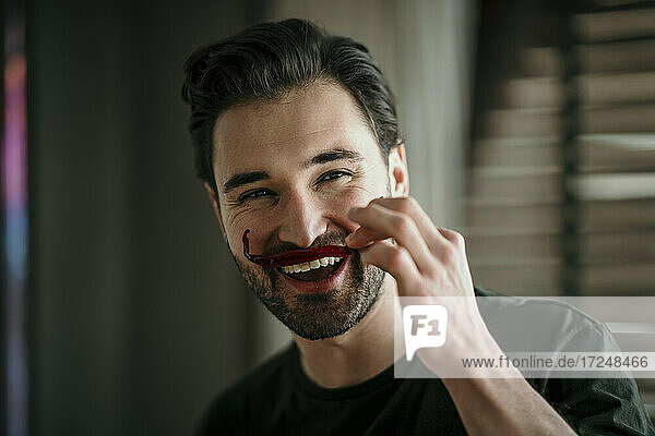 Lächelnder Mann imitiert Schnurrbart mit rotem Chili