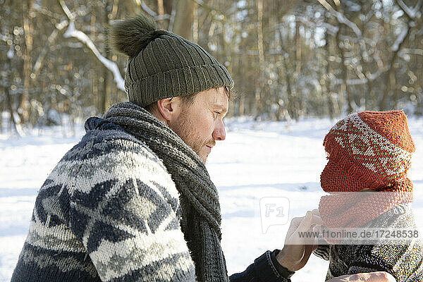 Father in warm clothing holding knit hat of son during winter