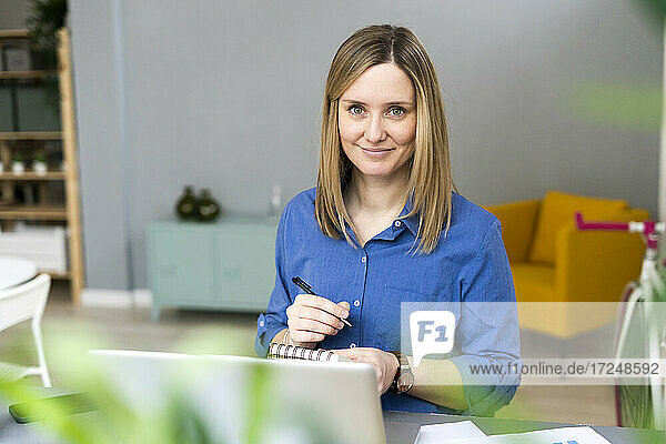 Smiling businesswoman writing in note pad at desk in office