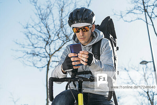 Zusteller  der sich auf ein Fahrrad stützt  während er sein Smartphone benutzt
