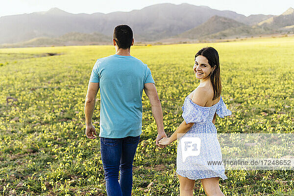 Lächelnde Frau hält die Hand eines Mannes beim Spaziergang auf einer Wiese