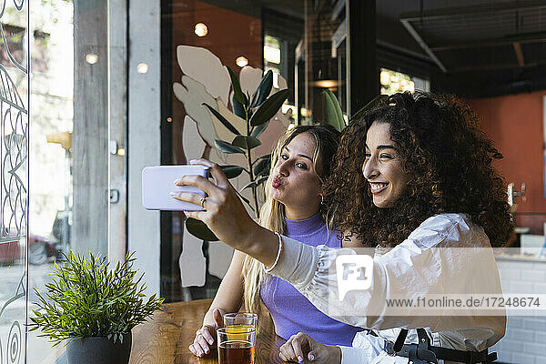 Fröhliche junge Freundinnen  die ein Selfie machen  während sie am Tisch im Restaurant sitzen