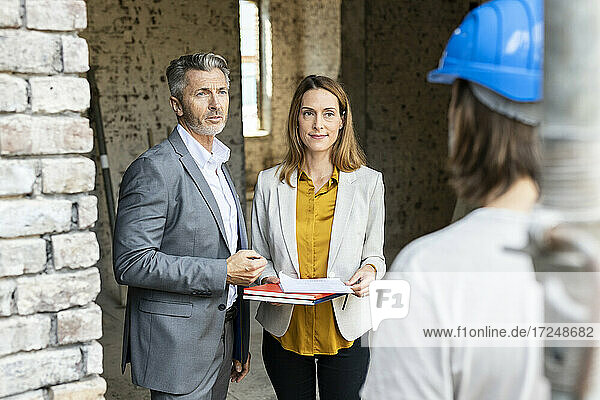 Male and female architect talking with construction worker at site