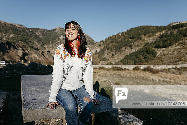Entspannte Frau sitzt auf einem Felsen im Gebirge