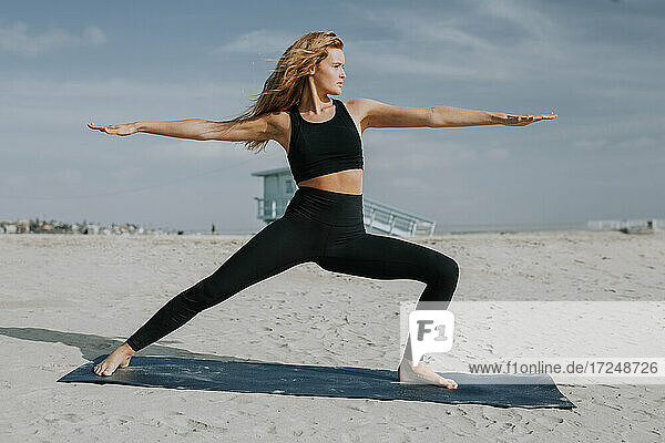 Woman exercising on mat at beach during sunny day