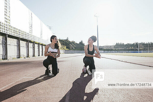 Lächelnde Freundinnen  die bei Sonnenschein auf dem Trainingsgelände hocken
