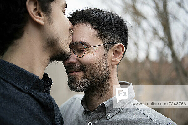 Mid adult man kissing on forehead of male friend outdoors