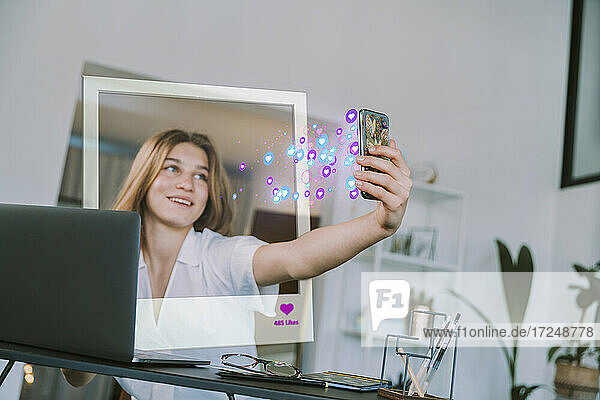 Weibliche Teenager-Influencerin  die mit ihrem Handy ein Selfie mit einem Symbol für soziale Medien zu Hause macht