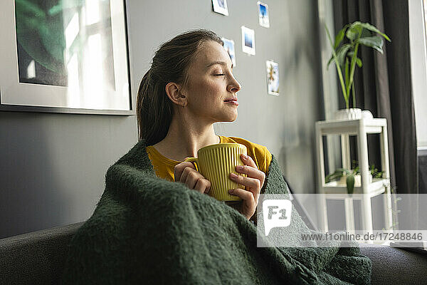 Frau in Decke eingewickelt mit Kaffeetasse zu Hause