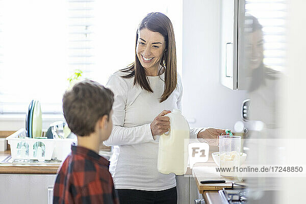 Smiling woman talking with son while preparing milkshake in kitchen