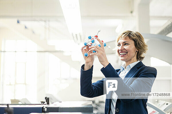 Smiling female expertise holding molecular structure model while standing in factory