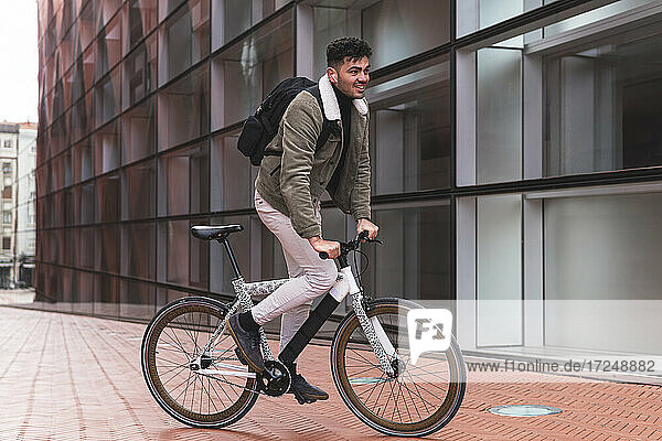 Male professional with backpack riding bicycle outside office building
