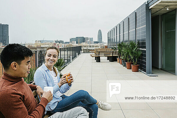 Lächelnde männliche und weibliche Fachkräfte unterhalten sich bei einem Kaffee auf dem Dach