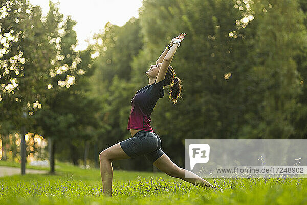 Junge Frau  die in einem öffentlichen Park Yoga in der Kriegerpose praktiziert
