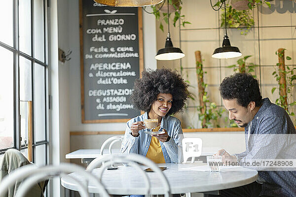 Weibliche Fachkraft trinkt Kaffee  während sie mit einem männlichen Kunden in einem Cafe sitzt