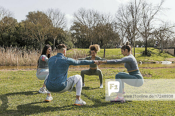 Male and female friends doing squatting exercise in public park