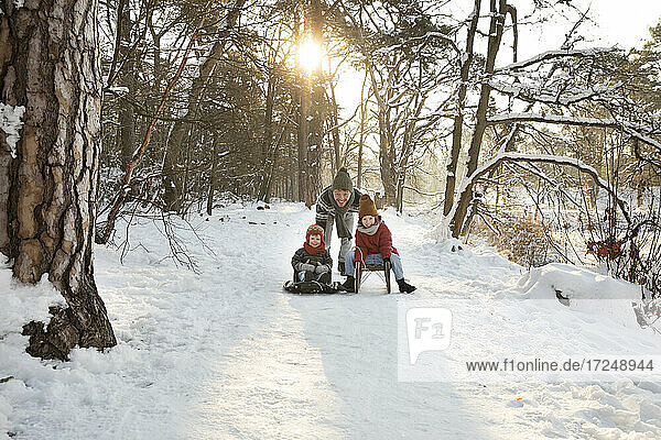 Father pushing sons sitting on sled during winter