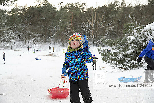 Playful boy with toboggan standing on snow