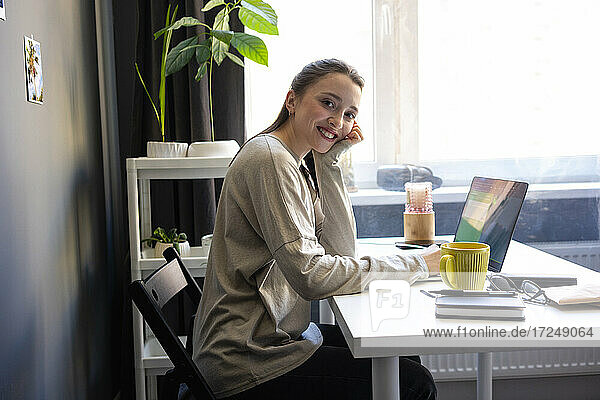 Smiling woman sitting by laptop at home office
