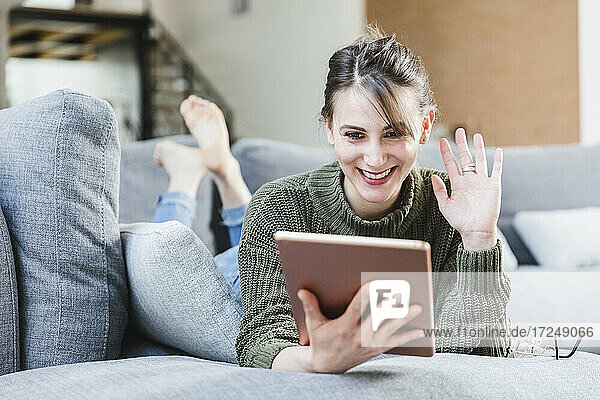 Junge Frau winkt während eines Videoanrufs auf einem digitalen Tablet zu Hause