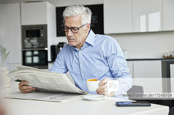Älterer Geschäftsmann mit Kaffeetasse  der in einer Cafeteria Zeitung liest