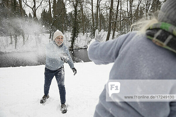 Playful man throwing snow on woman during winter
