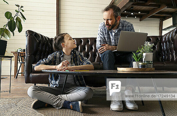 Vater mit Laptop bespricht sich mit seinem Sohn  während er zu Hause sitzt