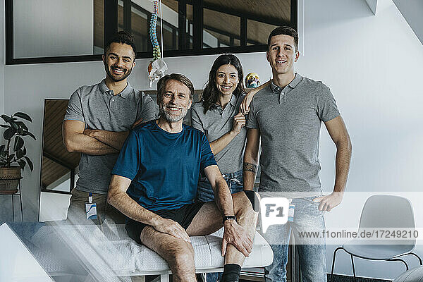 Smiling physiotherapists standing behind male patient in practice
