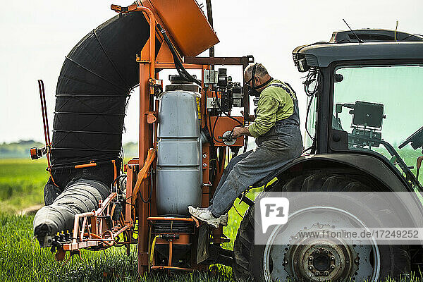 Älterer Landwirt mit Gesichtsmaske bei der Kontrolle eines Pestizidbehälters im Traktor