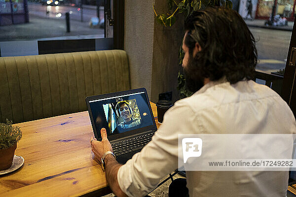 Junger Mann unterhält sich mit einem Freund über einen Videoanruf am Laptop im Restaurant