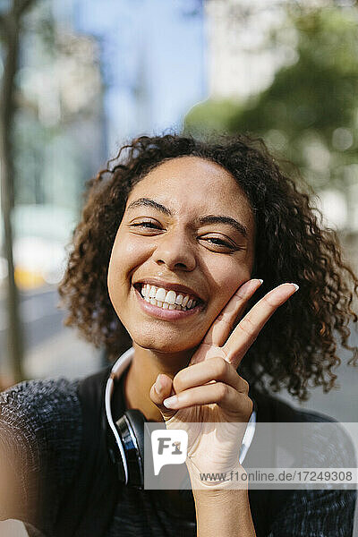 Cheerful woman showing peace sign in city
