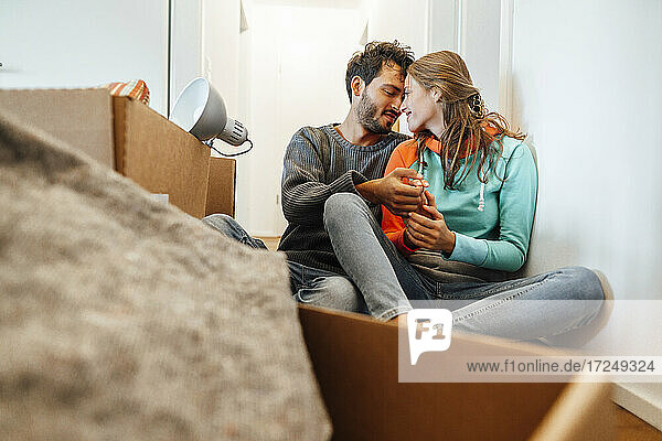 Young man embracing woman while sitting by box at home