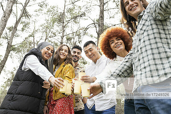 Lächelnder junger Mann  der ein Selfie macht  während er bei einer Party im Wald mit Gläsern anstößt