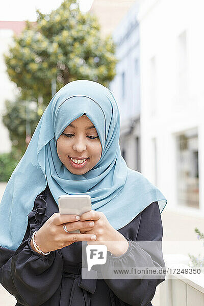 Junge Frau mit blauem Hidschab und Smartphone