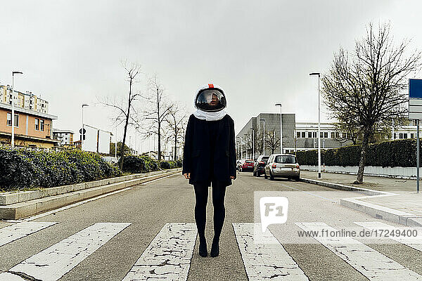 Frau mit Weltraumhelm auf Zebrastreifen an Straße stehend