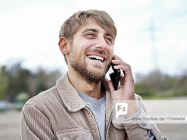 Happy bearded man looking away while talking on smart phone