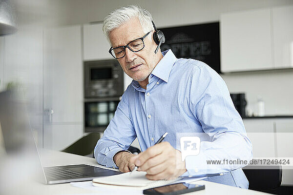 Male professional with wireless headset writing in book at office